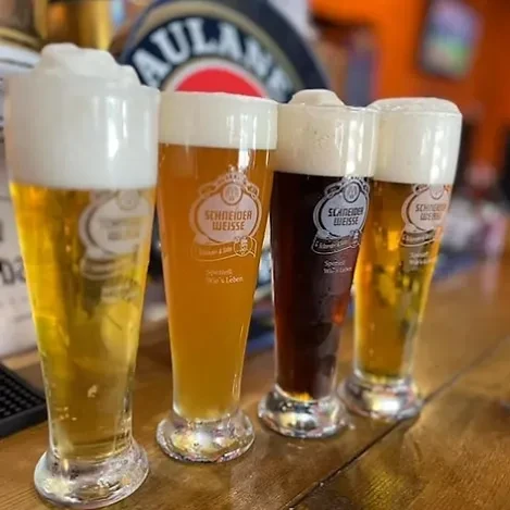 Four glasses of different Schneider Weisse beers on a wooden bar.