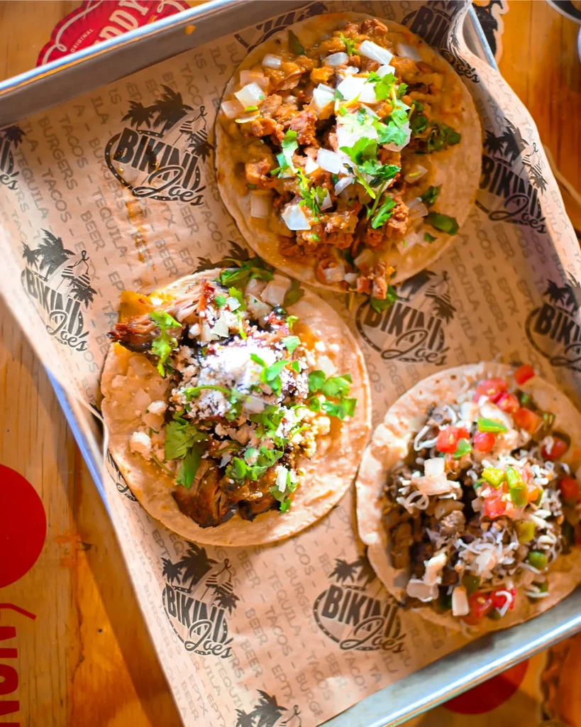 Three tacos with various toppings on a Bikini Joe's tray.