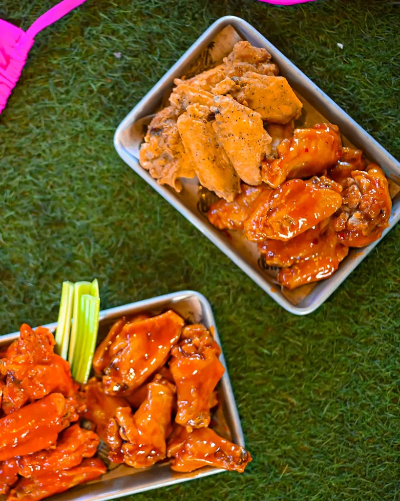 Two trays of chicken wings, some breaded, some sauced, on green turf.