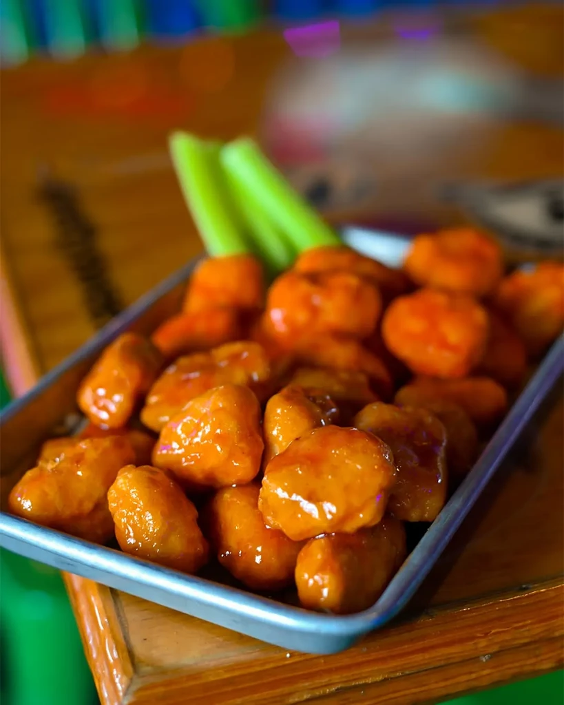Orange-sauced boneless chicken wings in a metal tray with celery.
