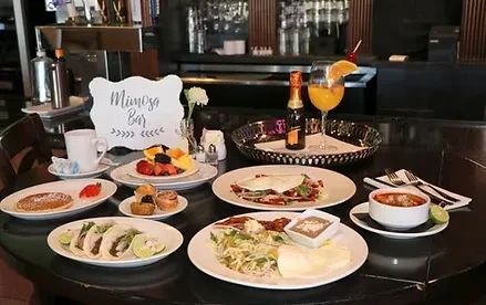 Brunch table with Mimosa Bar sign, pancakes, tacos, and mimosas.
