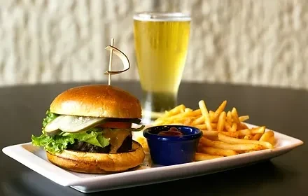 A hamburger, golden fries, ketchup, and amber beverage on a table.