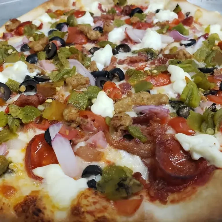 Close-up of a generously topped pizza with meats, fresh cheeses, and vegetables.