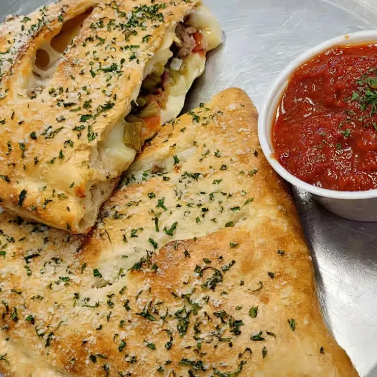 Golden calzone, cut open, revealing cheese, meat, vegetables, and marinara.