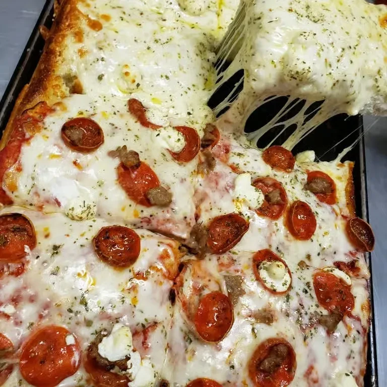 Spatula lifts a square pizza slice with pepperoni, sausage, and cheese pull.