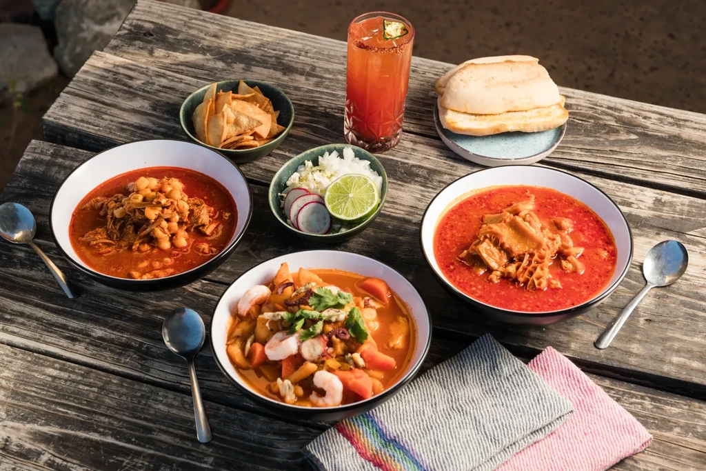 Three traditional stews, sides, and drink on a rustic wooden table.