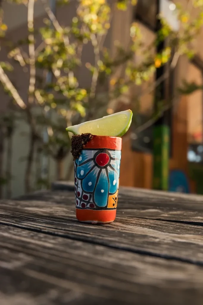 Colorful shot glass with spiced rim and lime on weathered wood.