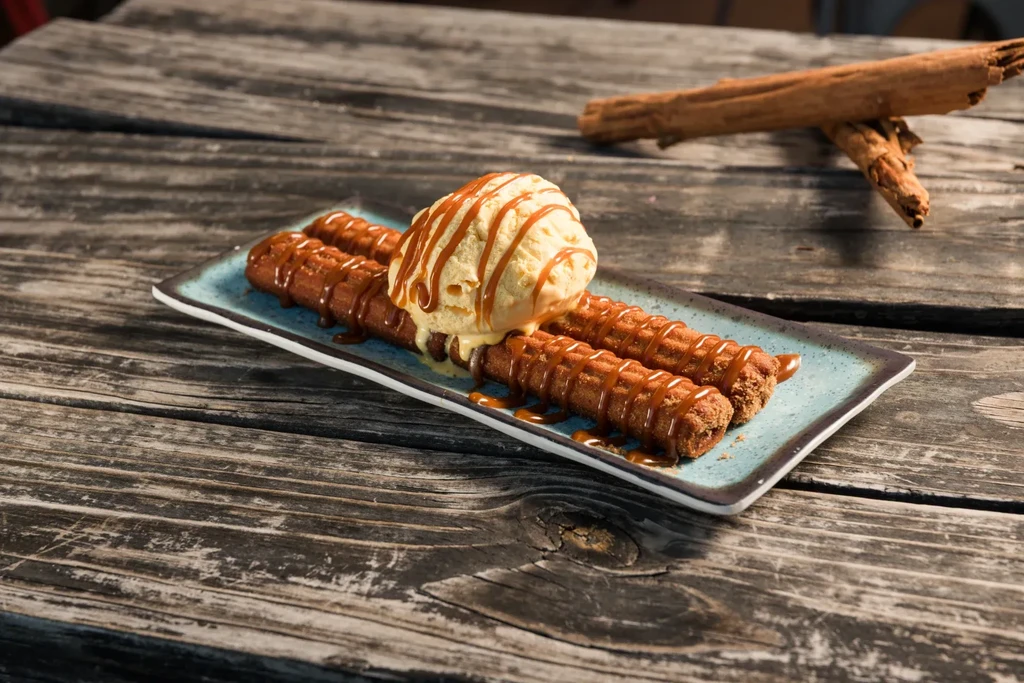 Three churros, vanilla ice cream, and caramel on a rustic wooden table.