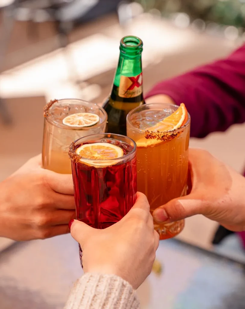 Several hands hold colorful, chili-salt rimmed drinks and a beer bottle.