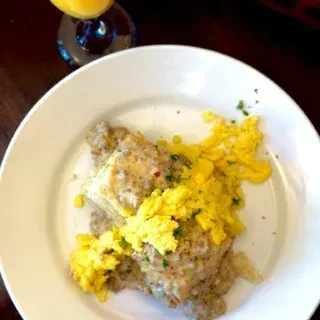 Biscuits with sausage gravy, scrambled eggs, and orange juice on a white plate.
