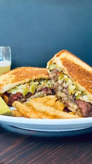 Toasted sandwich with grilled meat, cheese, fries, and pickle.