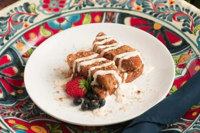 French toast with icing, berries, and cinnamon on a patterned tablecloth.