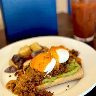 Avocado toast with spiced meat, two poached eggs, and roasted potatoes.