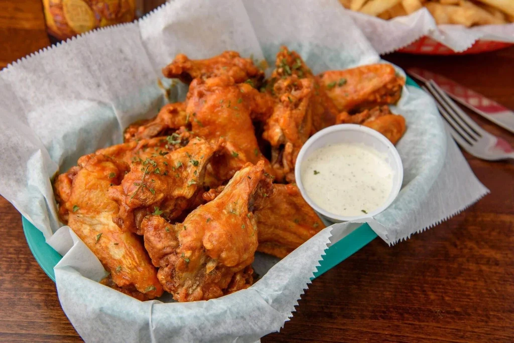Buffalo wings with creamy dip and herbs in a turquoise basket.