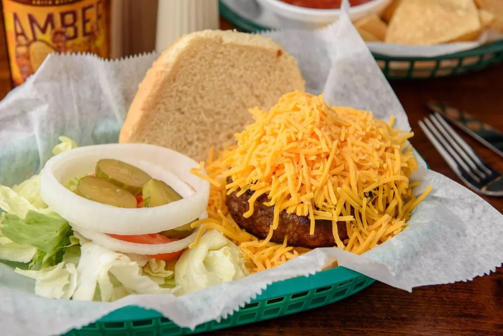 Cheesy beef patty with burger toppings and bun in a green basket.