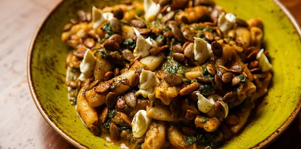 Gnocchi with dark sauce, pumpkin seeds, and cheese, in a green bowl.