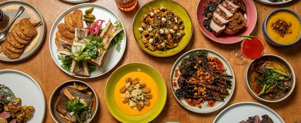 Overhead shot of a wooden table laden with diverse, plated food and drinks.