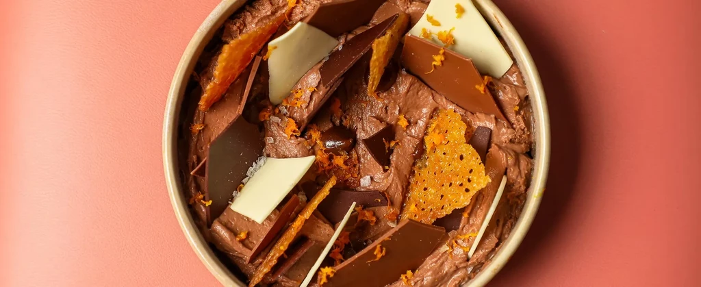 Creamy chocolate dessert with chocolate pieces, orange zest, and a wafer.