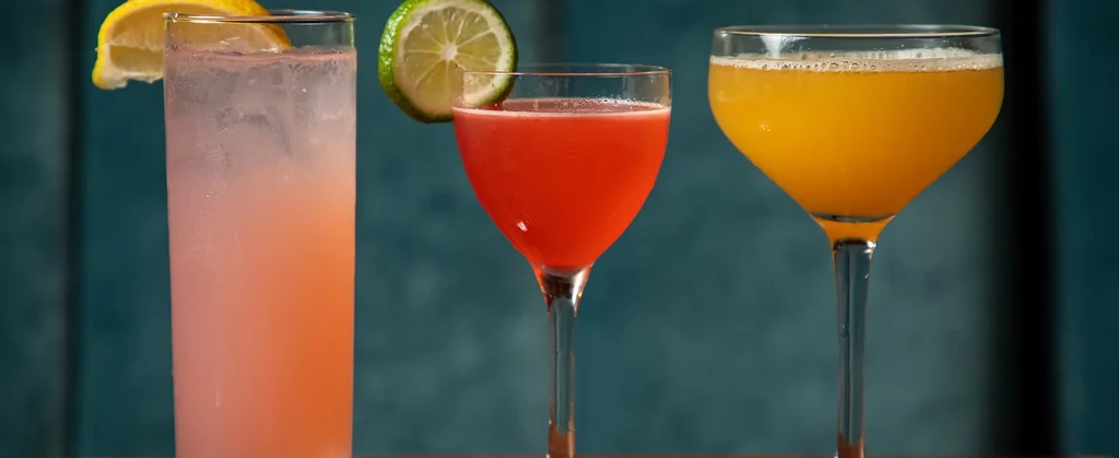 Professionally styled pink, red, and orange cocktails on a dark surface.