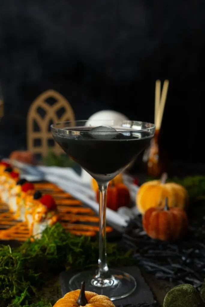 Black martini cocktail, sushi, and pumpkins in a spooky Halloween setting.