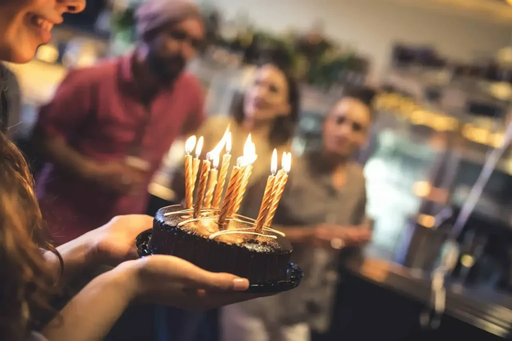 Chocolate cake with many lit spiral candles held by hands.
