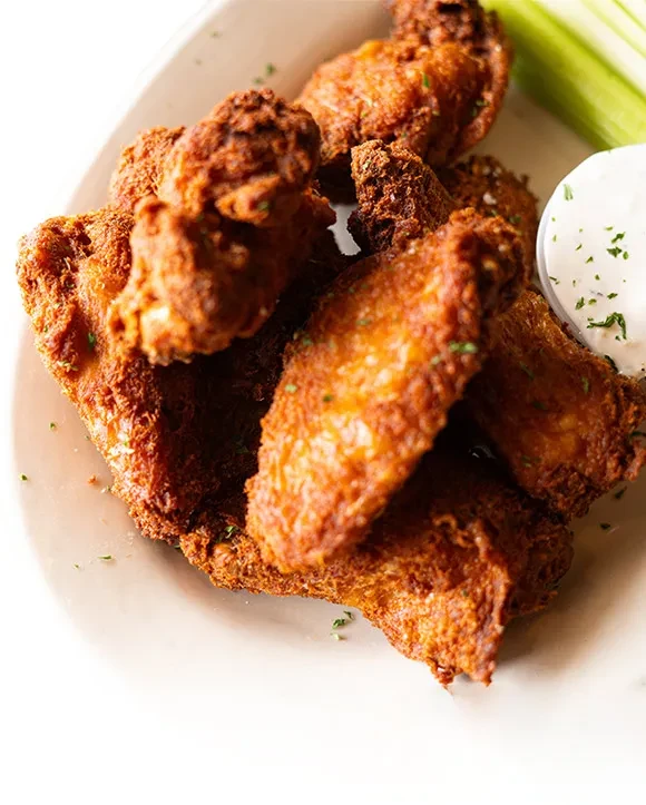 Piled golden-brown crispy fried chicken wings, dipping sauce, and celery.