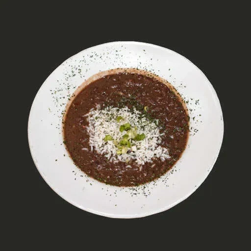 Overhead dark stew topped with crumbled white cheese and green onions.