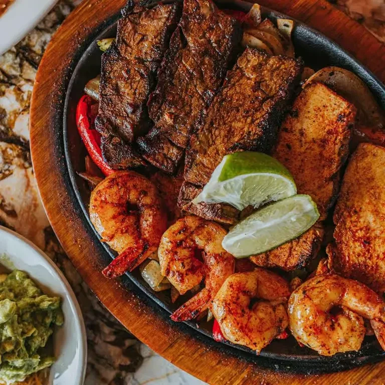 Sizzling cast iron skillet with grilled steak, shrimp, chicken, vegetables, lime.