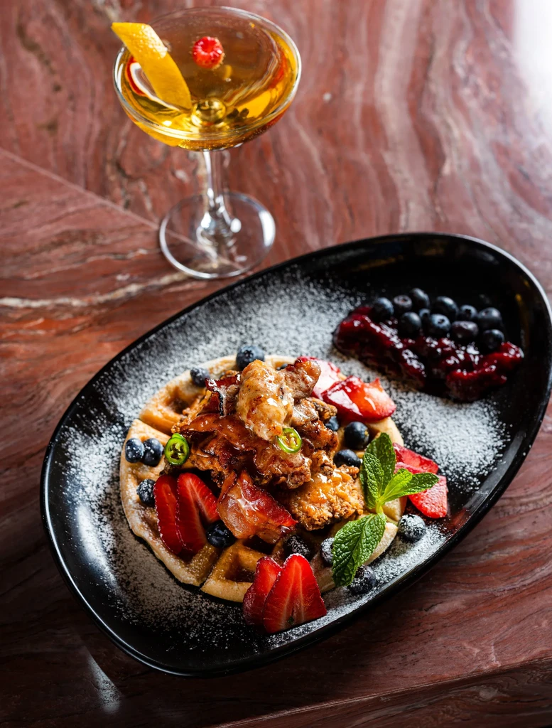 Crispy chicken and bacon waffle with berries and an amber cocktail.