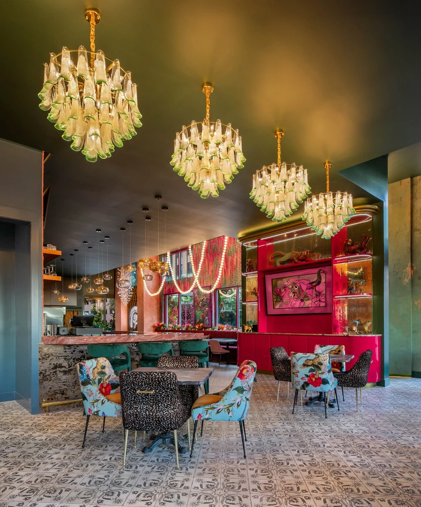Opulent restaurant interior: bottle chandeliers, green ceiling, red walls, patterned chairs.