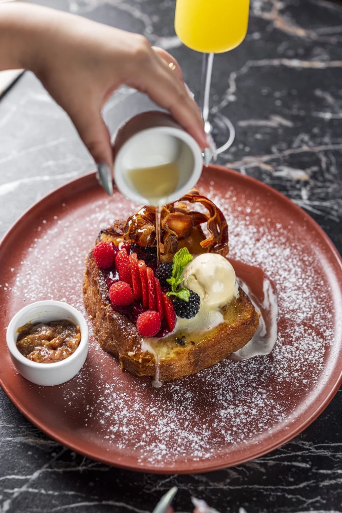 French toast with berries, ice cream, candied bacon, and pouring syrup.