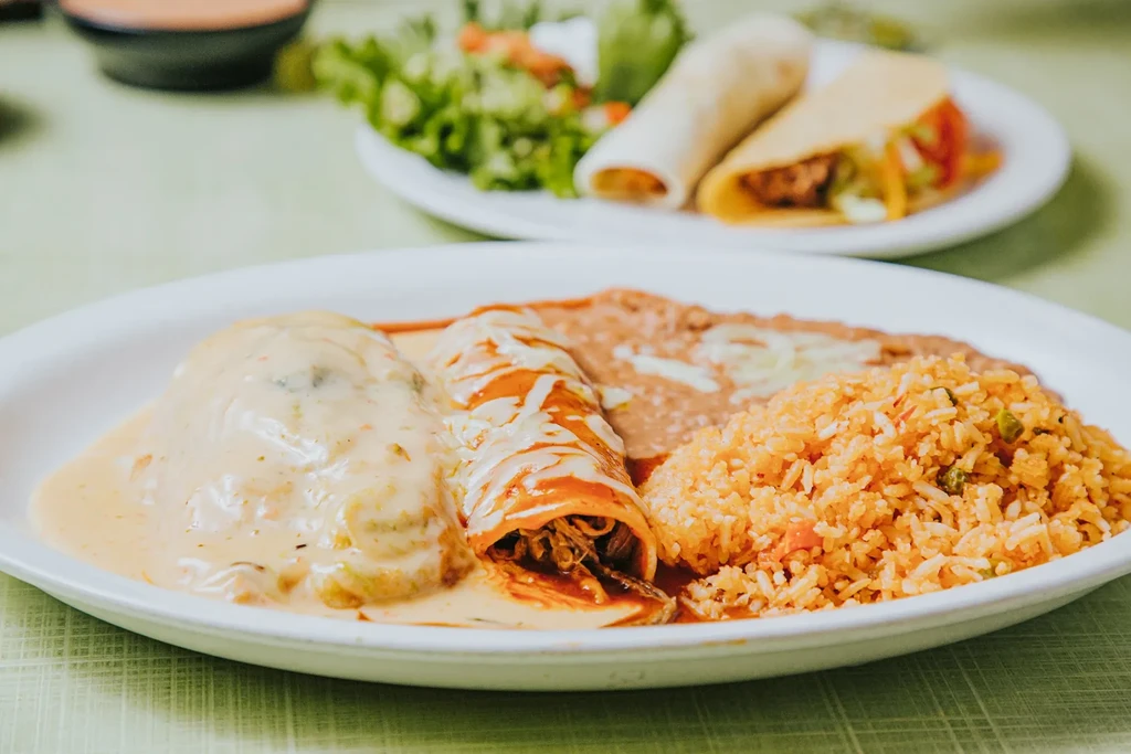 Close-up: Two enchiladas with sauces, refried beans, and rice.
