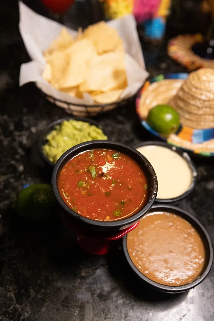 Assortment of Mexican dips, tortilla chips, and a decorative sombrero.