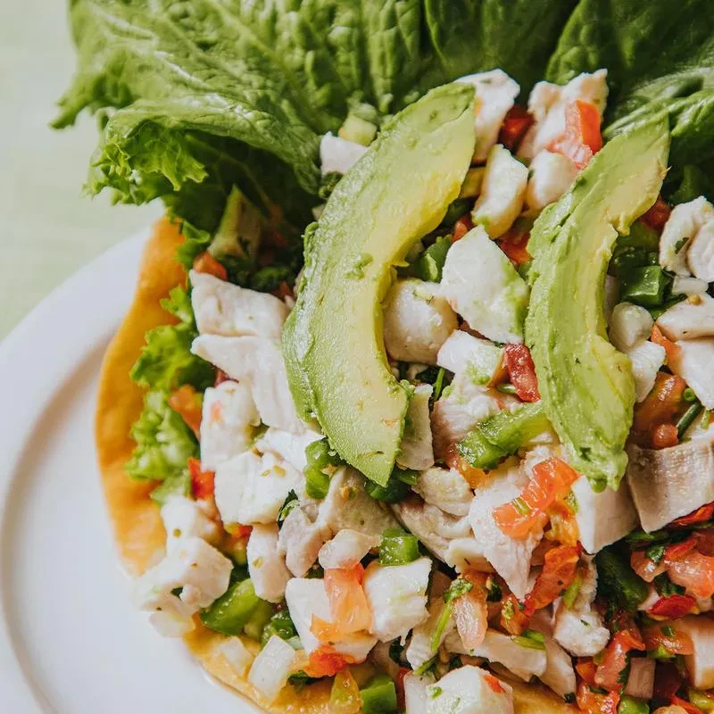 Colorful seafood ceviche topped with avocado, served on a tostada.