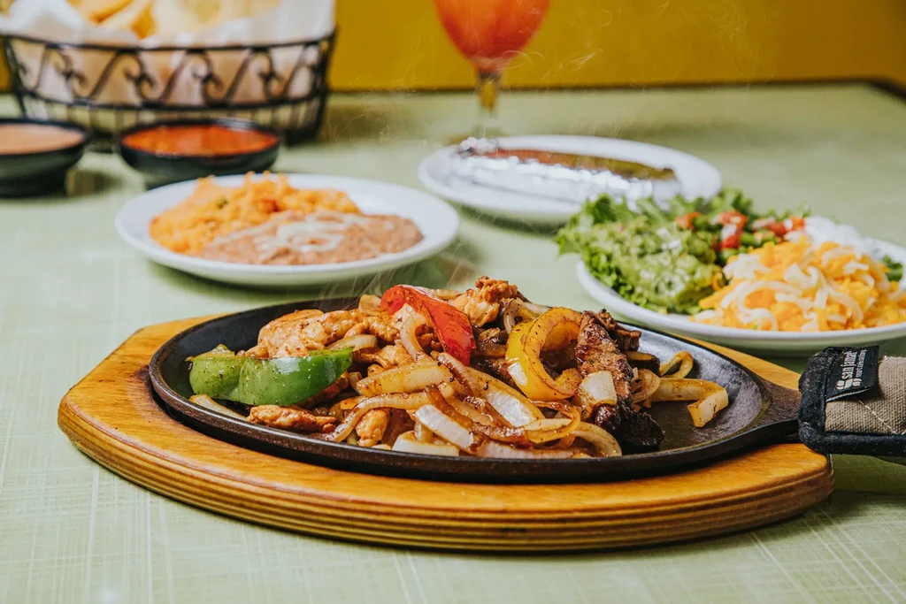 Sizzling chicken and beef fajitas with sides, sauces, and lime.