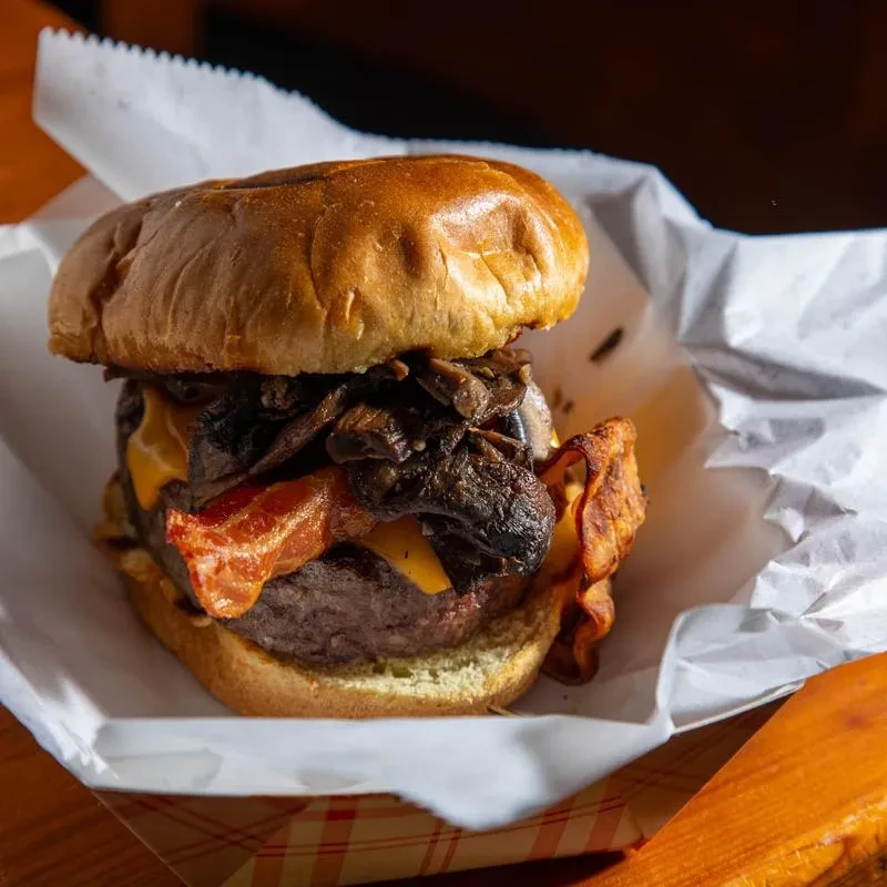 Gourmet beef burger with cheese, bacon, mushrooms, served in a checkered tray.
