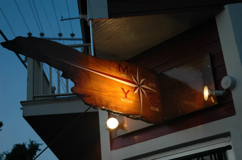 Illuminated wooden sign for "Mid City Yacht Club" with a compass rose.