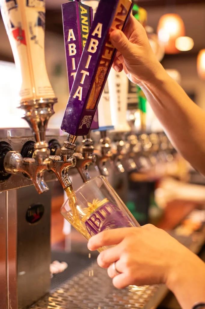 Hands pouring Abita beer from a tap into an Abita glass.