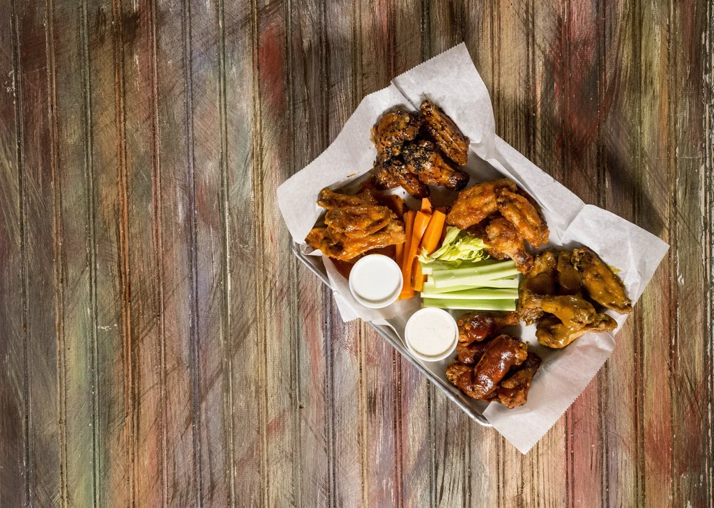 Overhead: Chicken wings, carrots, celery, and dips on rustic wood.