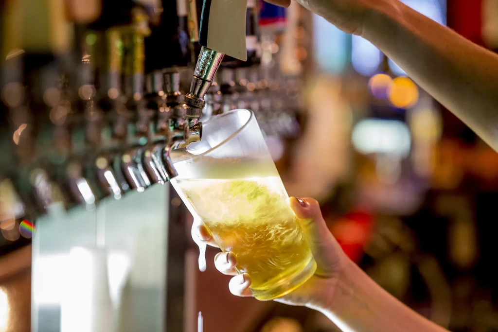 Hand holds glass as frothy golden beer pours from tap.