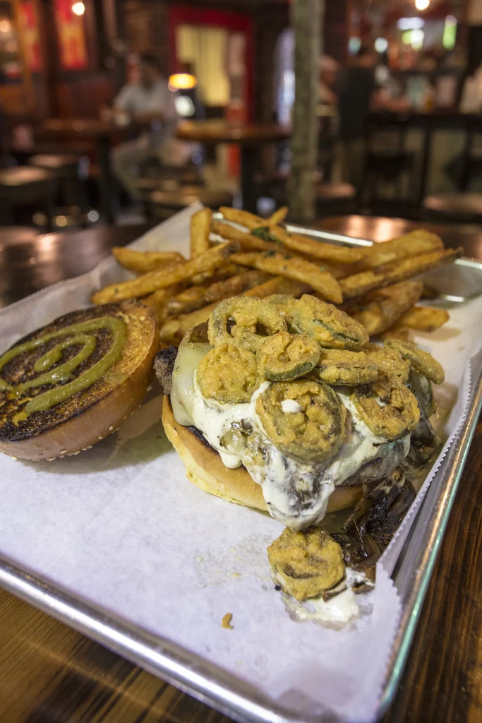 Gourmet burger with fried pickles, thick fries, served on metal tray.