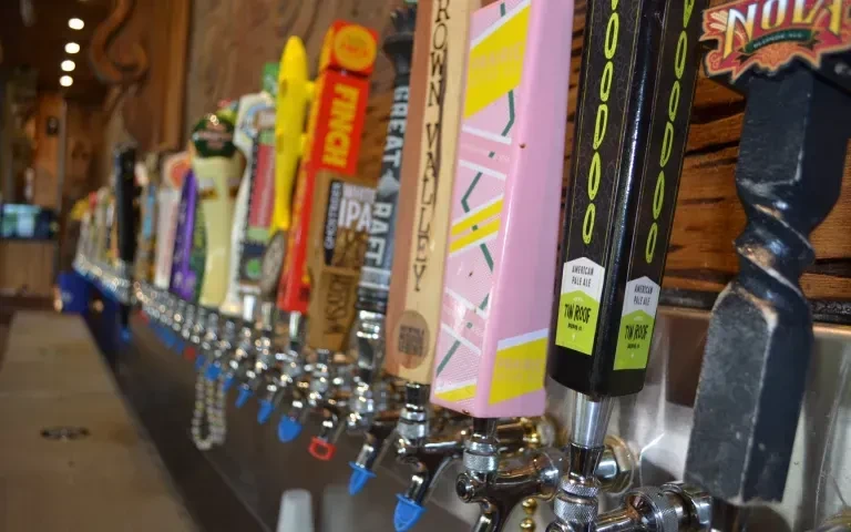Close-up of colorful, branded beer tap handles on a bar.