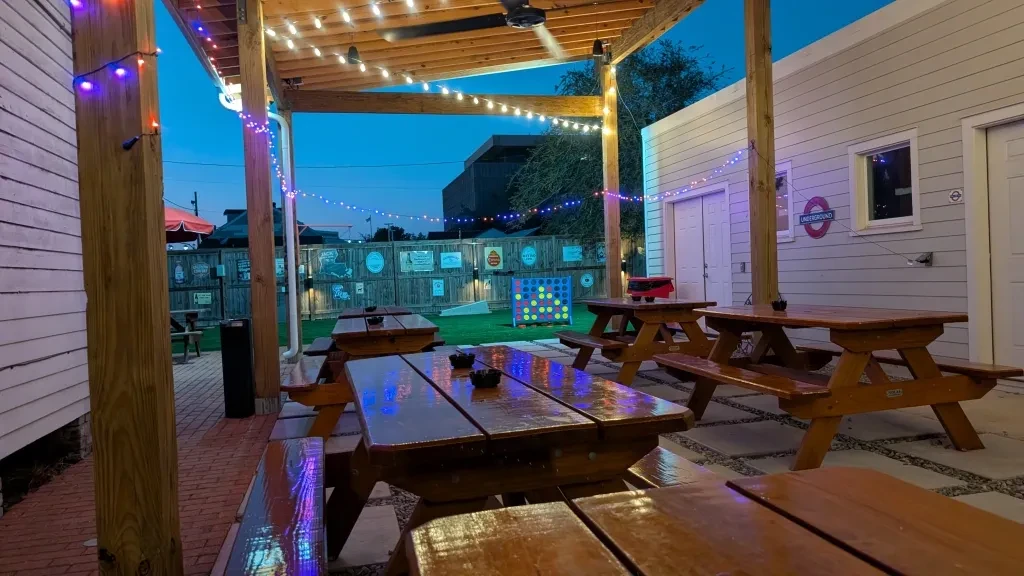 Nighttime beer garden with picnic tables, string lights, and Connect Four.