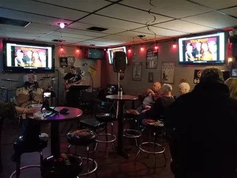 Dimly lit bar with live band on stage and karaoke on TVs.