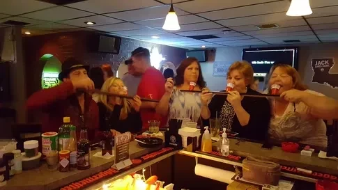Five people drinking shots from a wooden plank at a bar.