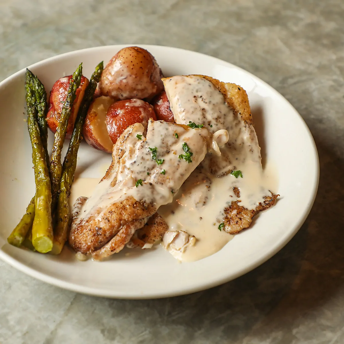 Fish in cream sauce with asparagus and red potatoes on plate