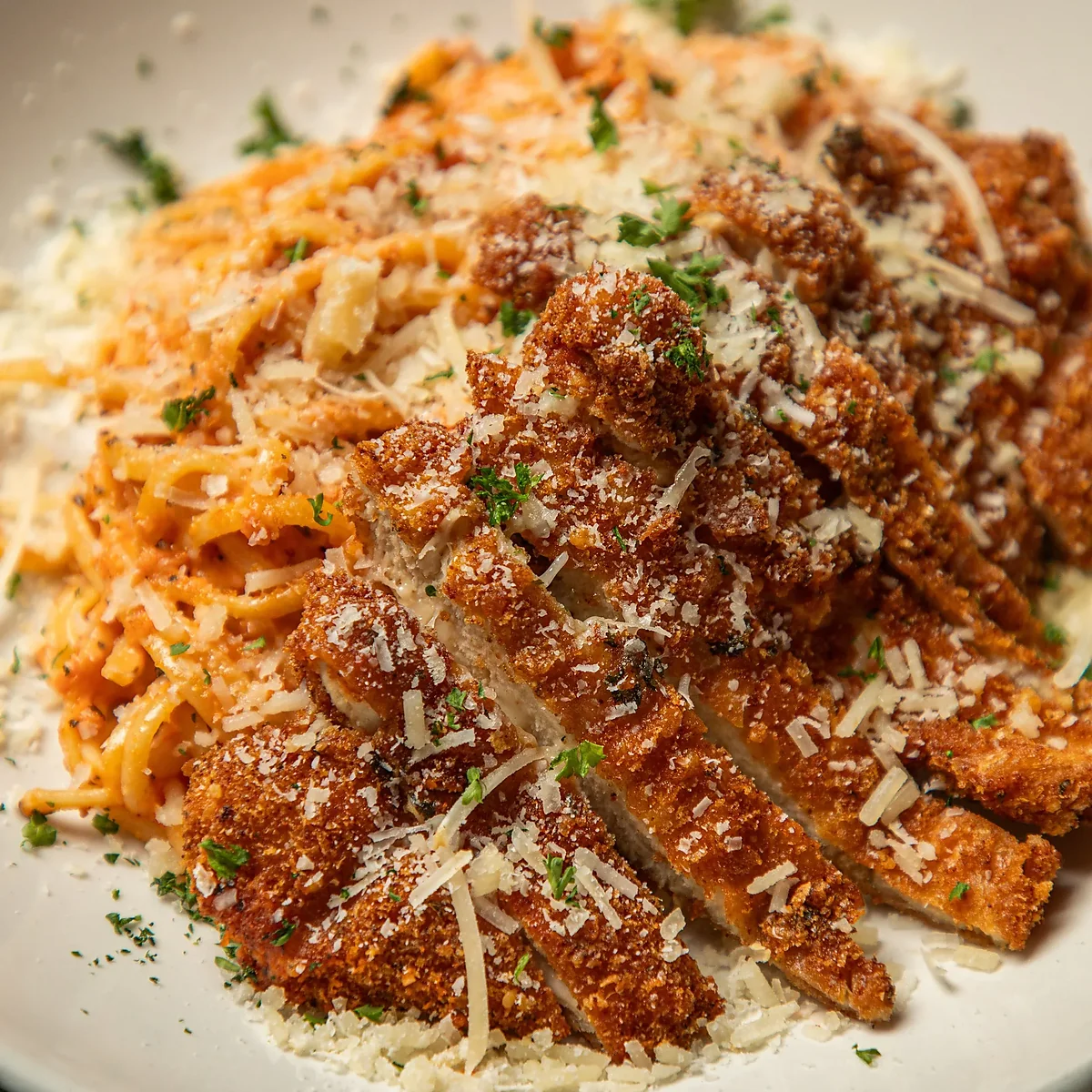 Sliced breaded chicken cutlet over pasta with tomato cream sauce
