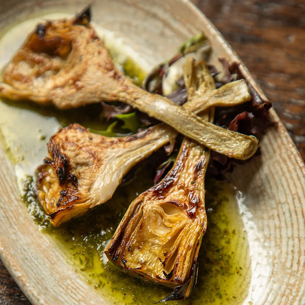 Grilled artichoke hearts with herb oil and greens on plate