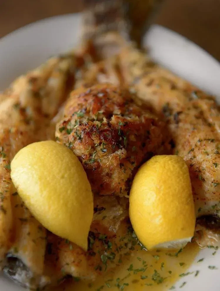 Baked fish with herbed crust, stuffing, and lemon halves on white plate.