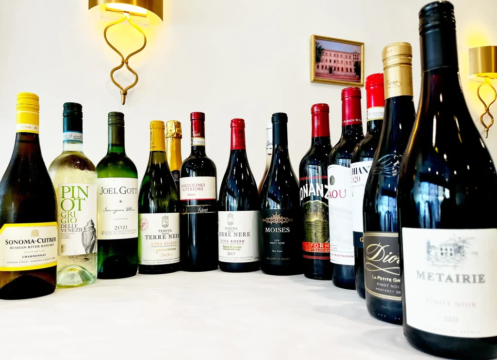 Fifteen assorted red, white, and sparkling wine bottles on a white surface.